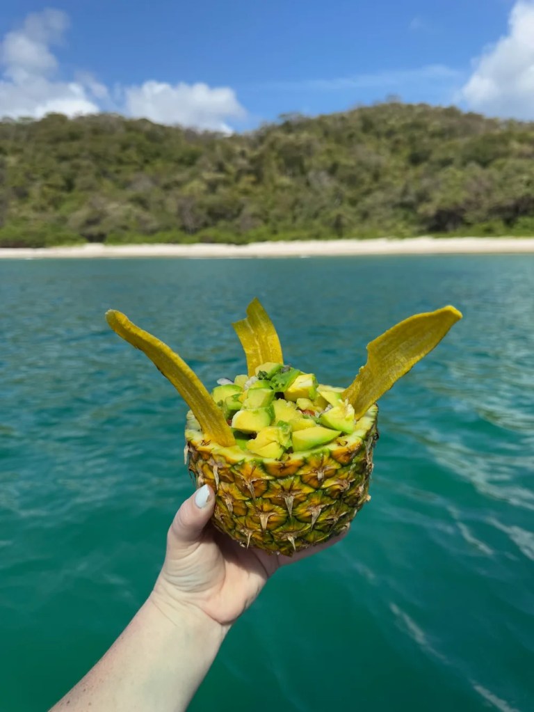 Fresh ceviche in a pineapple being held over the ocean