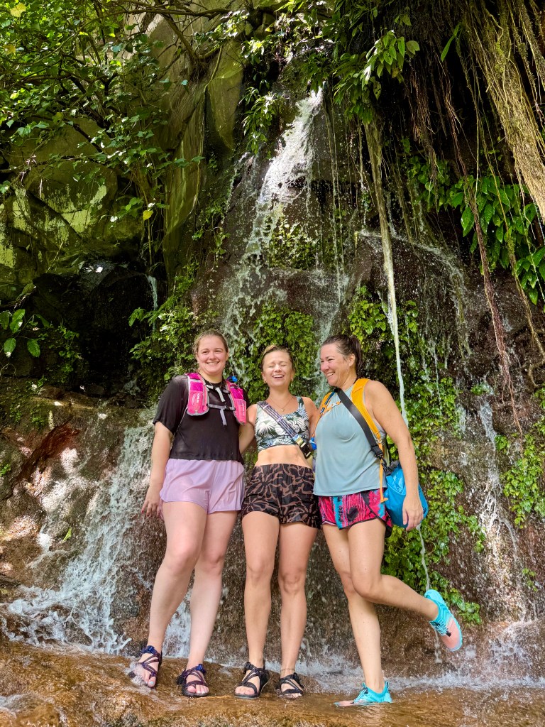 Three women standing under a waterfall in El Salvador