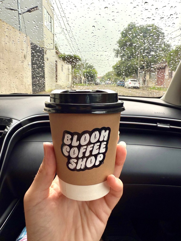 Woman holding a latte in a cup reading bloom coffee shop